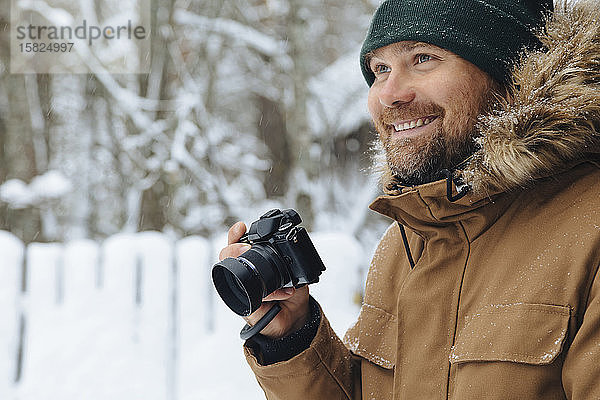 Porträt eines glücklichen Mannes mit Digitalkamera im Winter
