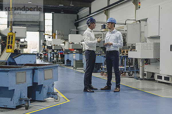 Zwei Männer mit Schutzhelmen unterhalten sich in einer Fabrik