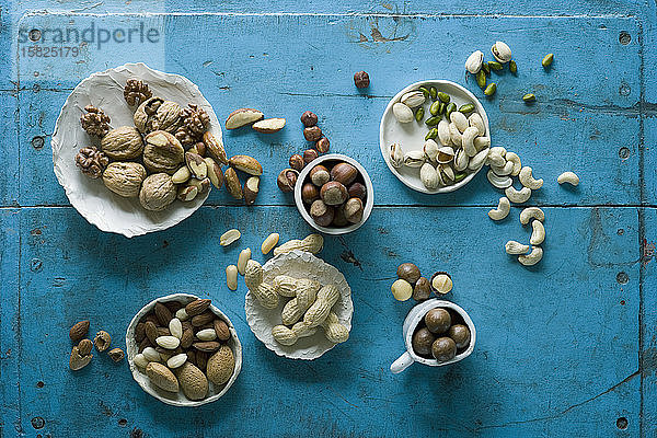 Draufsicht auf verschiedene Nüsse in Schalen auf blauem rustikalem Tisch