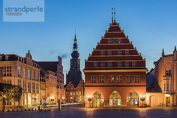 Deutschland  Mecklenburg-Vorpommern  Greifswald  Beleuchtetes Rathaus in der Abenddämmerung mit dem Turm des Heiligen Nikolai im Hintergrund