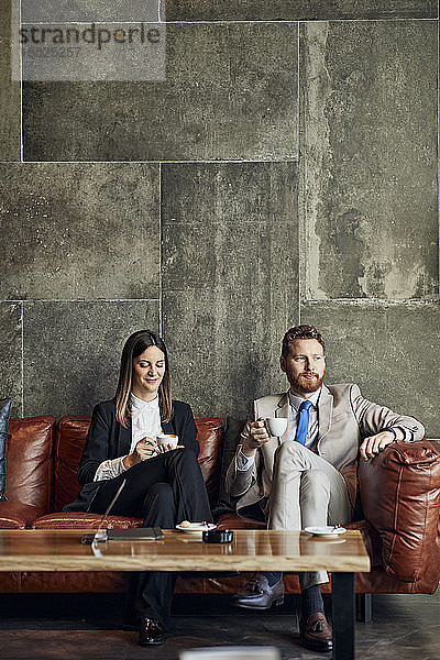 Geschäftsmann und Geschäftsfrau sitzen auf der Couch in der Hotellobby und machen eine Kaffeepause