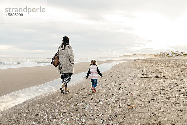 Rückansicht von Mutter und Tochter beim Spaziergang am Strand bei Sonnenuntergang