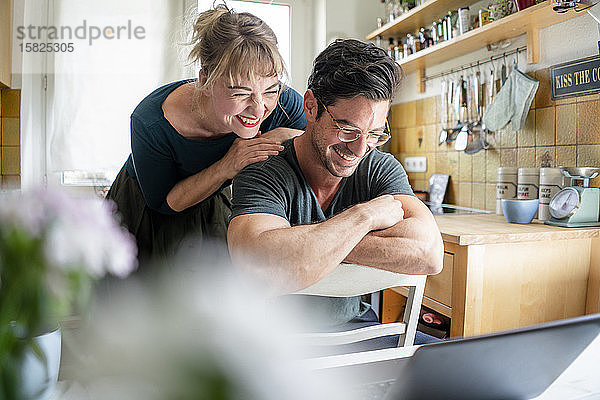 Glückliches Paar in der Küche schaut auf den Laptop