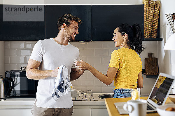 Glückliches junges Paar beim gemeinsamen Abwasch in der Küche zu Hause