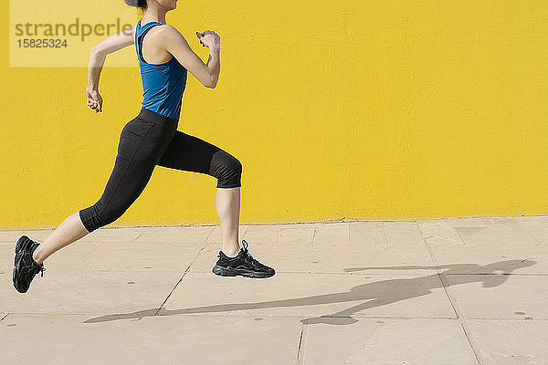 Junge Frau joggt vor einer gelben Wand