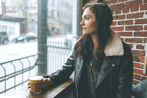 Frau mit einem Kaffee  die in einem Café aus dem Fenster schaut