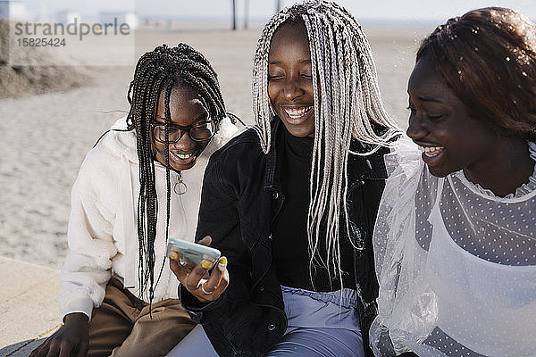 Glückliche Teenager-Freundinnen mit Smartphone am Strand