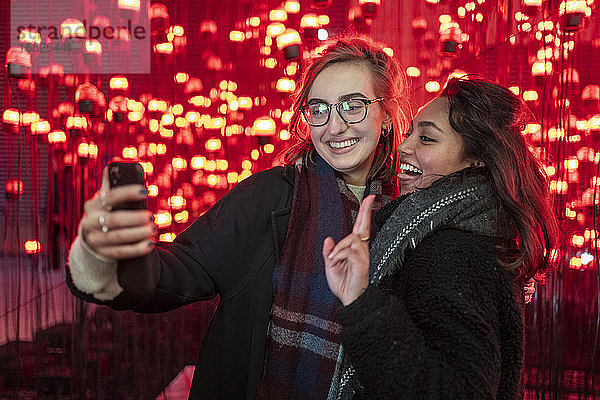 Porträt von glücklichen Freunden  die vor roten Glühbirnen ein Selfie machen