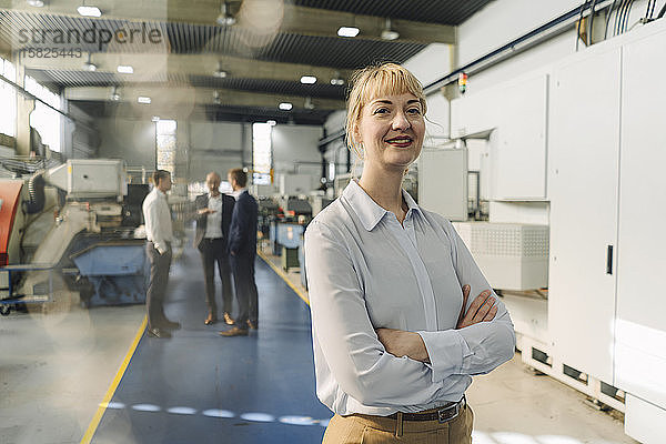Porträt einer selbstbewussten Geschäftsfrau in einer Fabrik mit Kollegen im Hintergrund