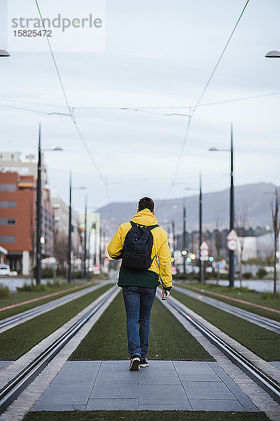 Rückansicht eines Mannes mit Rucksack in der Stadt auf Straßenbahnschienen
