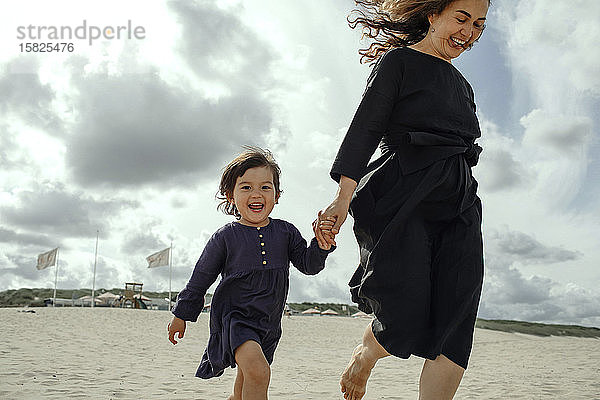 Porträt eines glücklichen kleinen Mädchens  das Hand in Hand mit seiner Mutter am Strand geht  Den Haag  Niederlande
