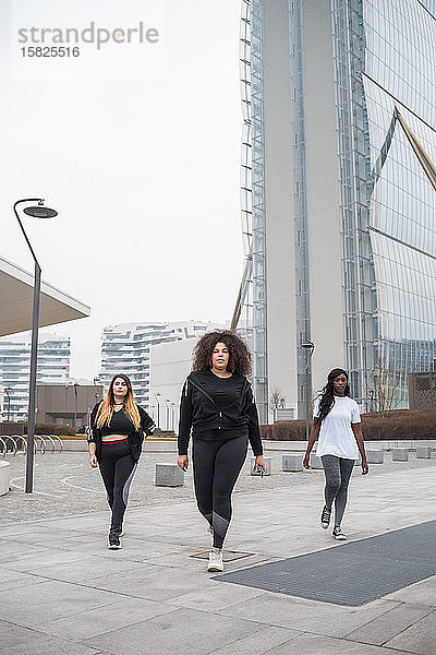Drei sportliche junge Frauen gehen in der Stadt spazieren