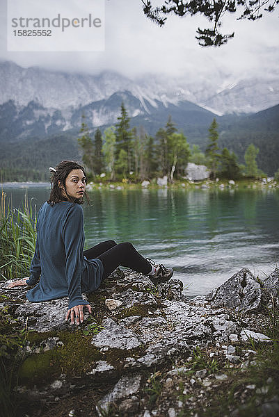 Deutschland  Bayern  Eibsee  Porträt einer jungen Frau  die auf einem Felsen am Ufer des Eibsees in den bayerischen Alpen sitzt