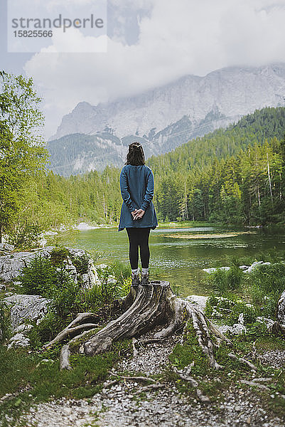 Deutschland  Bayern  Eibsee  Junge Frau steht auf einem Baumstumpf am Frillensee in den Bayerischen Alpen