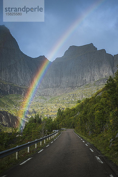 Norwegen  Lofoten  Regenbogen über leerer Straße in Berglandschaft