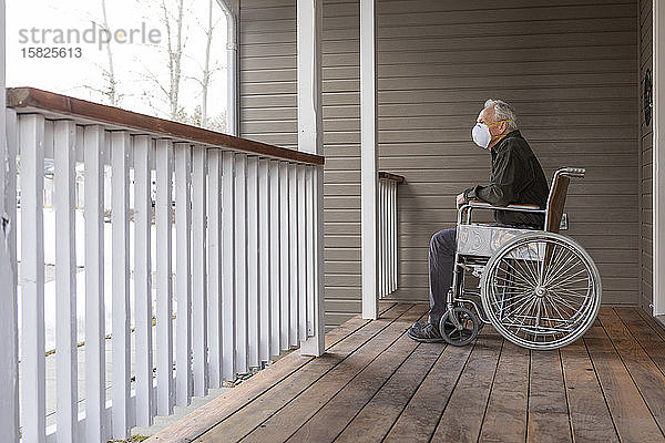 Älterer Mann im Rollstuhl trägt auf der Veranda eine Schutzmaske  um die Übertragung des Coronavirus zu verhindern