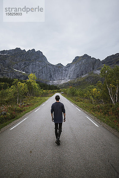 Norwegen  Lofoten-Inseln  Mann geht Straße in Berglandschaft entlang
