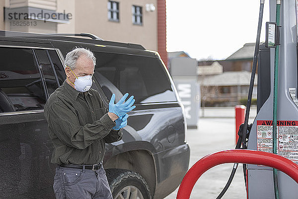 Mann mit OP-Handschuhen und Maske an einer Tankstelle