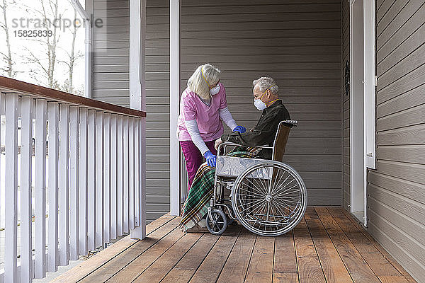Frau und Mann im Rollstuhl tragen auf der Veranda eine Schutzmaske  um die Übertragung des Coronavirus zu verhindern