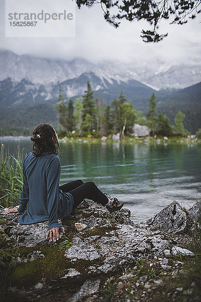 Deutschland  Bayern  Eibsee  Junge Frau sitzt auf einem Felsen am Ufer des Eibsees in den bayerischen Alpen