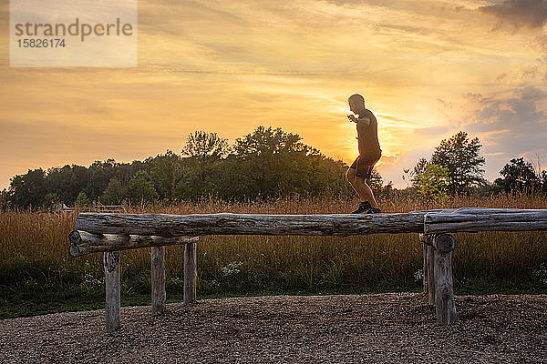 Ein Mann geht über einen Balken im Freien als Silhouette gegen den Sonnenuntergang