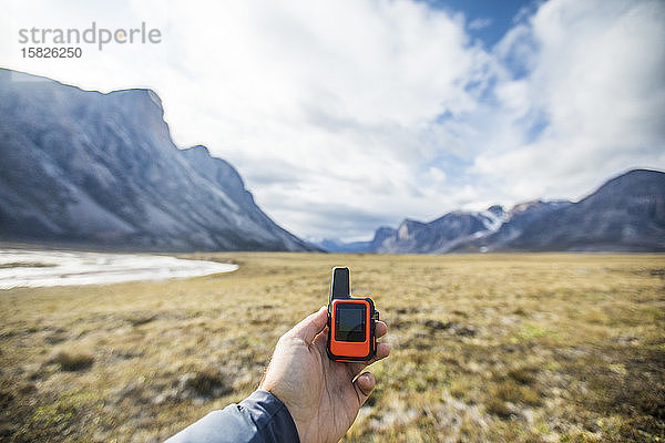 Abenteurer hält ein Mini-GPS und ein satellitengestütztes Sicherheitskommunikationsgerät.