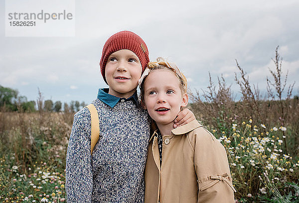 Bruder und Schwester stehen sich im Herbst umarmend in einem Feld mit Wildblumen