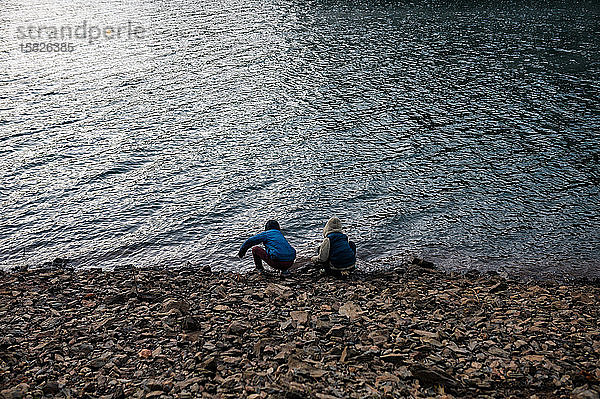 Zwei Kinder hocken auf Felsen am Rande eines Sees