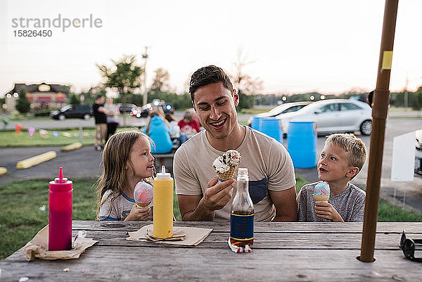 Junger Mann und Kinder essen am Sommerabend Eis am Picknicktisch