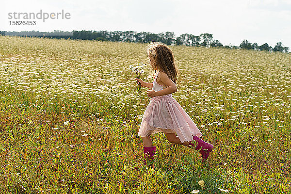 Kleines Mädchen  das im Sommer in einem Blumenfeld rennt.