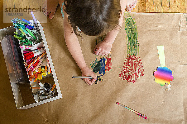 Draufsicht auf ein kleines Kind  das ein großes Wandgemälde mit bunten Blumen zeichnet