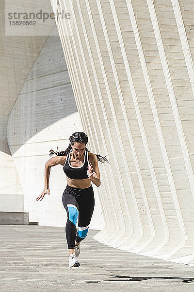 Ganzkörper einer Sportlerin in Sportkleidung  die auf Beton läuft