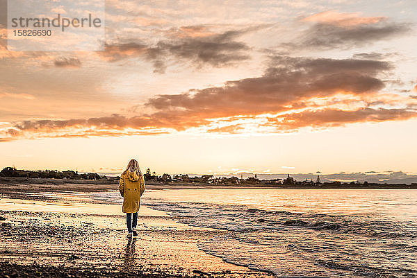Ein Mädchen  das im Winter in der Dämmerung am Strand spazieren geht