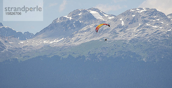 Gleitschirmflieger fliegen an einem sonnigen Tag hoch über schneebedeckten Bergen.