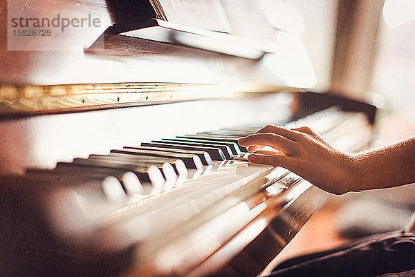 Ausgeschnittenes Bild einer Kinderhand  die in einem sonnigen Raum Klavier spielt.