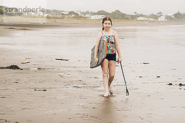Junges Mädchen geht mit ihrem Boogie-Board am Strand spazieren