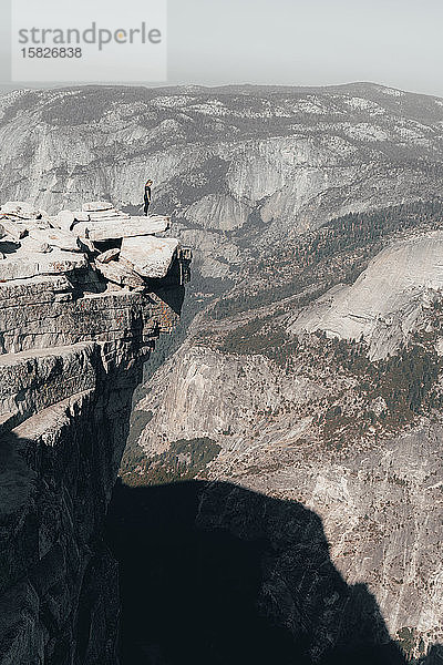 Junge Frau steht auf der Spitze des Half Dome und schaut über eine Klippe