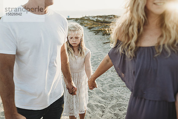 Ernsthaftes Mädchen mit traurigem Gesicht beim Spaziergang mit den Eltern am Strand