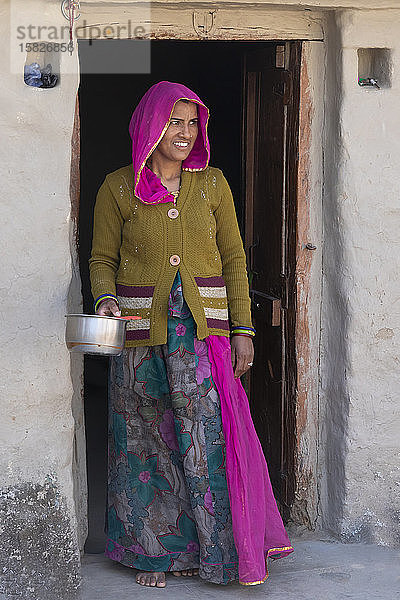 In Indien hält eine Frau in traditioneller Kleidung in einer Türöffnung einen Topf.