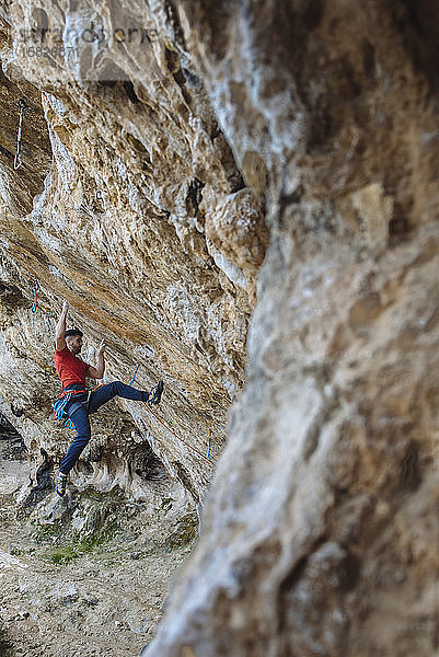 Bergsteiger  der eine harte Route in einer Sportkletterhöhle beginnt.