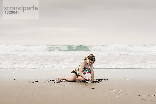Junges Mädchen sitzt und spielt am Strand