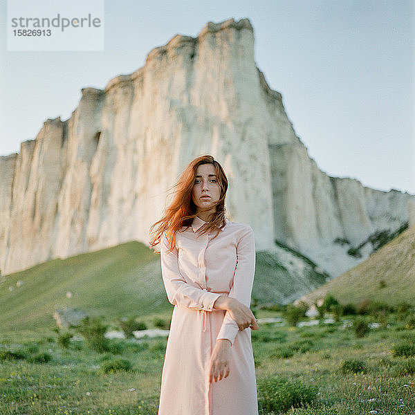 Attraktive Frau mit roten Haaren steht in der Nähe des Berges