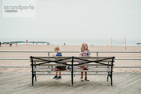 Zwei Kinder essen an einer Strandpromenade Eiscreme.