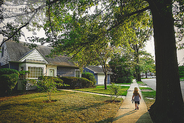 Ein kleines Mädchen geht auf einem Weg an einem blauen Haus vorbei.