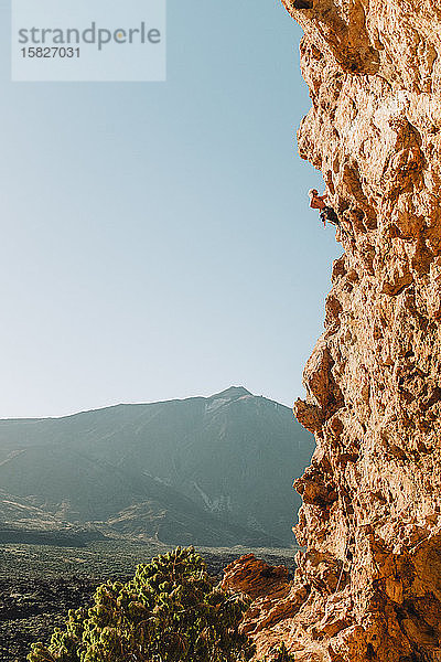 Rückansicht eines männlichen Kletterers an der Wand mit El Teide im Rücken