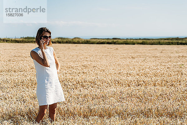 Eine fröhliche Frau telefoniert auf dem goldenen Grasfeld.