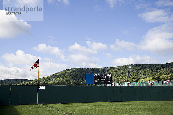 Baseball-Außenfeldzaun und Rollhügel mit Anzeigetafel und amerikanischer Flagge