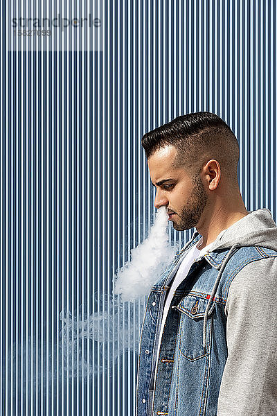 Junger Mann raucht mit einer elektronischen Zigarette auf blauem Hintergrund