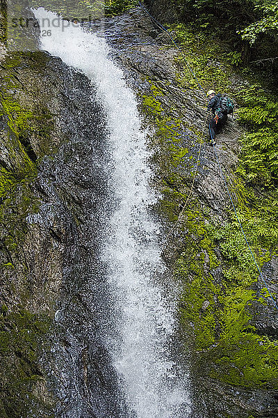 Seitenansicht eines Mannes  der sich neben einem Wasserfall im Canyon abseilt.