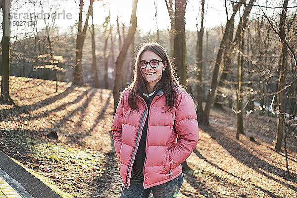 Glückliches junges Mädchen mit Brille  einer rosa Jacke und Jeans